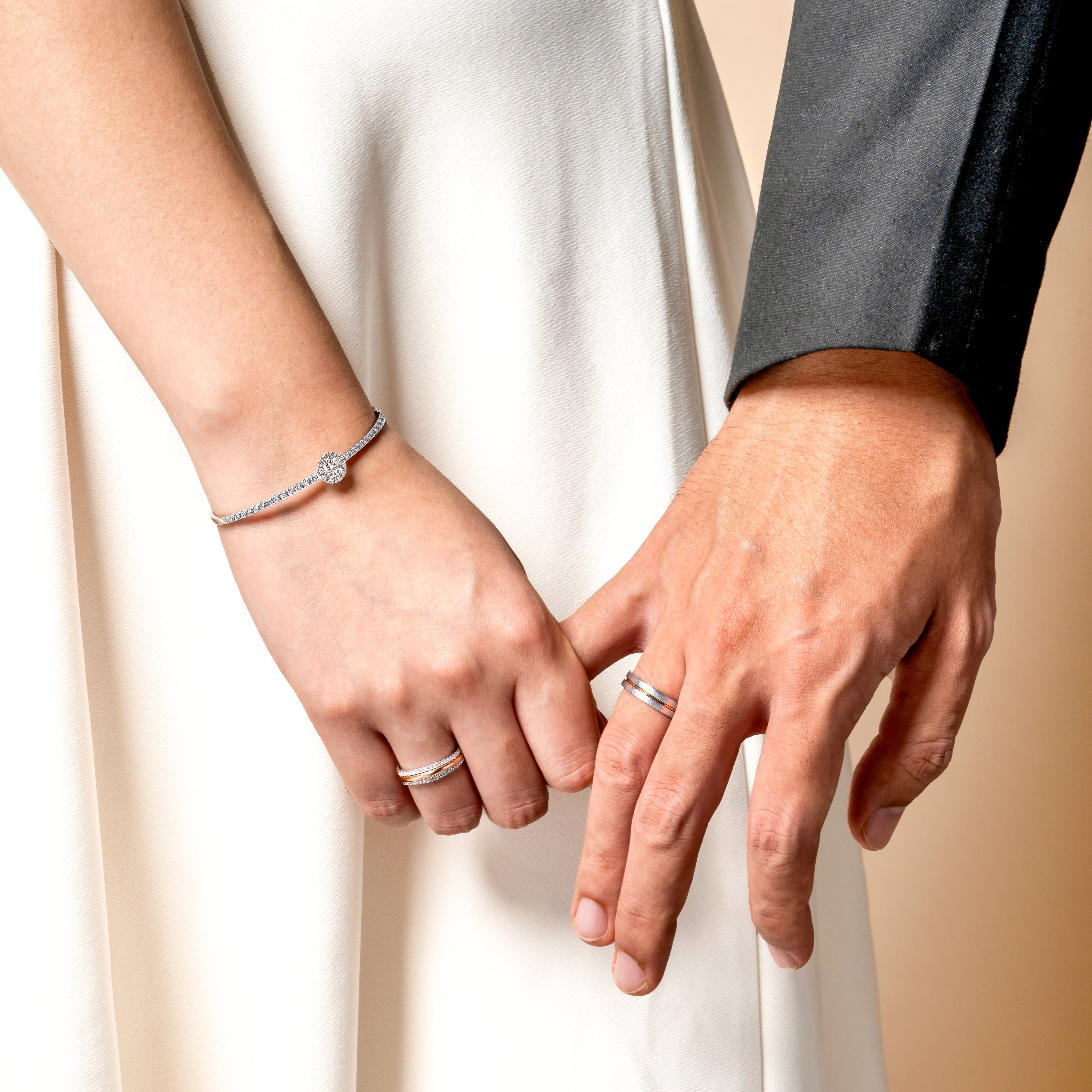 Two people holding hands with wedding rings against a plain background